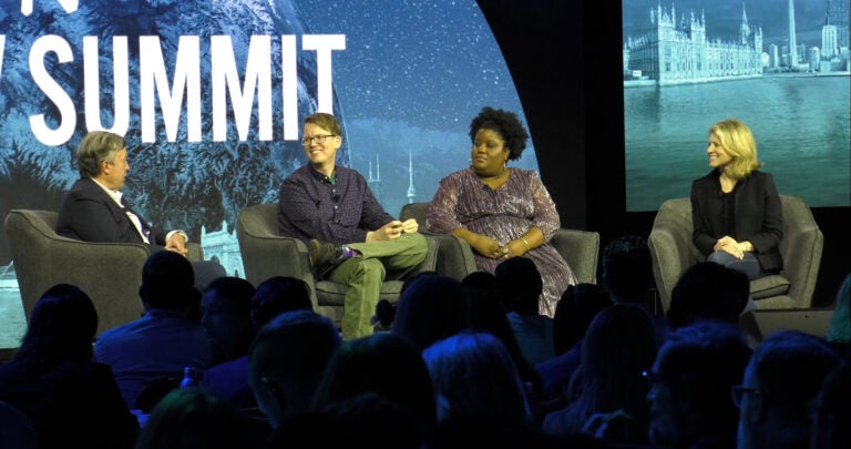 A panel discussion at an event with four people seated on a stage, in front of a backdrop displaying "SUMMIT."