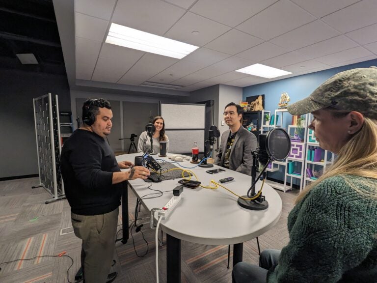 Four people around a table with microphones and audio equipment in a recording studio.